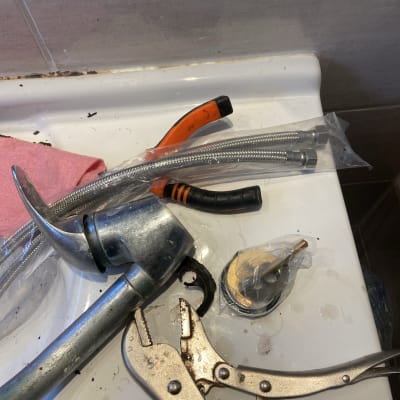 כלי עבודה של אינסטלטור על כיור, כולל מפתח צינורות וצינור גמיש