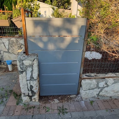 שער מתכת אפור עם מסגרת עץ ואבנים מסביב