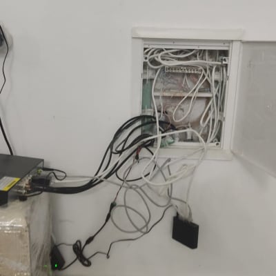 ארון תקשורת פתוח עם כבלים מחוברים ומכשיר רשת על שולחן.