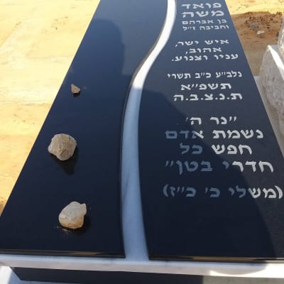 מצבה שחורה עם כיתוב בעברית ואבנים מונחות עליה
