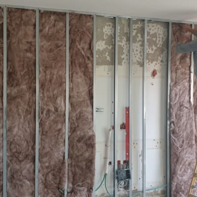 אדם מתקין לוחות גבס על קיר עם בידוד