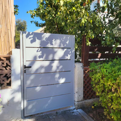 שער מתכת אפור עם ידית שחורה בכניסה לגינה