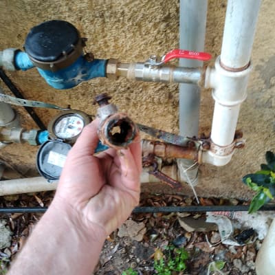 יד מחזיקה צינור חלוד ליד מד מים וברזים