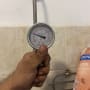 מד לחץ מים מוחזק ביד ליד צינור מתכת