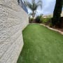 דשא סינטטי בחצר עם קיר אבן ועצים