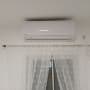 מזגן מותקן על קיר מעל חלון עם וילון לבן
