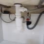 צנרת פלסטיק לבנה מתחת לכיור עם ברזים וצינורות