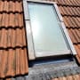 חלון גג מוקף רעפים חומים עם מסגרת מתכת