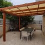 פרגולה מעץ עם שולחן וכיסאות בגינה מרוצפת