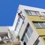 אדם צובע קיר חיצוני של בניין בעזרת חבלים