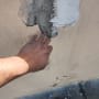 יד נוגעת בקיר עם טיח מתקלף ותיקון בטיח חדש