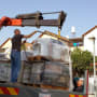A crane lifting pallets with construction materials on a truck.