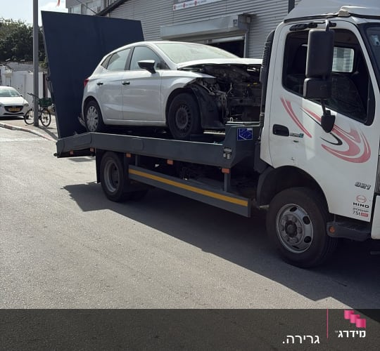 רכב על גרר מול מוסך עם שלט בעברית