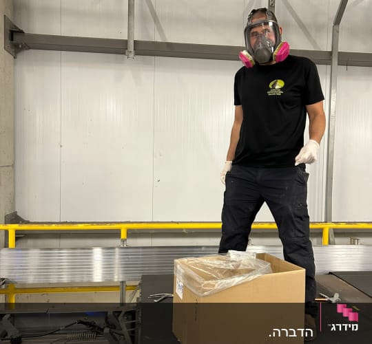 אדם עם מסכת מגן ליד קופסה על מסוע