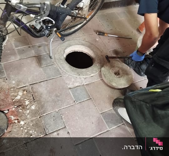 אדם פותח מכסה ביוב עם כלים