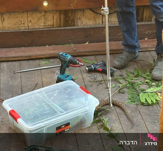 אדם מחזיק מוט עם נחש ליד כלי עבודה