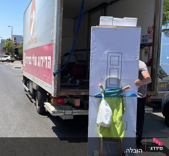 אדם מעביר קרטון גדול עם עגלה למשאית פתוחה