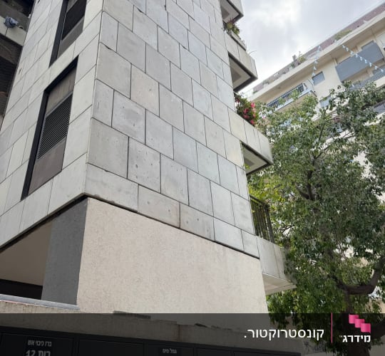 בניין מגורים עם תיבות דואר ועץ בצד