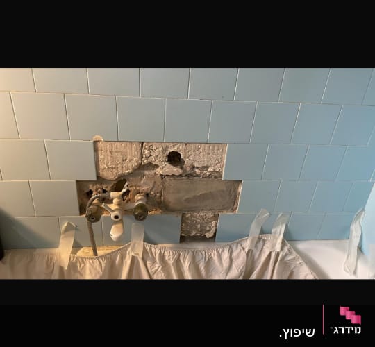 קיר עם אריחים שבורים וצנרת חשופה