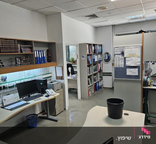 משרד עם שולחנות עבודה, מחשבים וספרים על מדפים