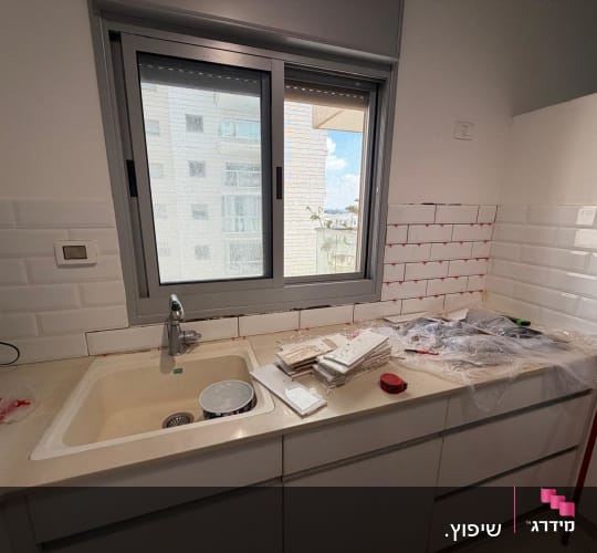 תהליך חיפוי קיר מטבח באריחי בריקים לבנים במהלך שיפוץ