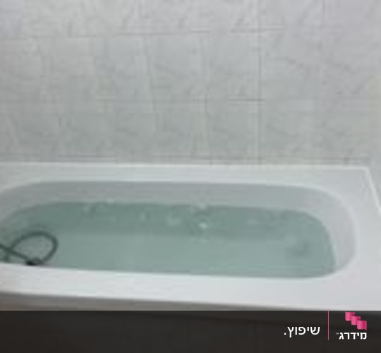 אמבטיה לבנה מלאה במים וקיר מחופה באריחי קרמיקה