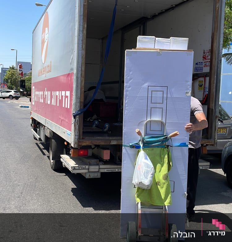 אדם מעביר קרטון גדול עם עגלה למשאית פתוחה