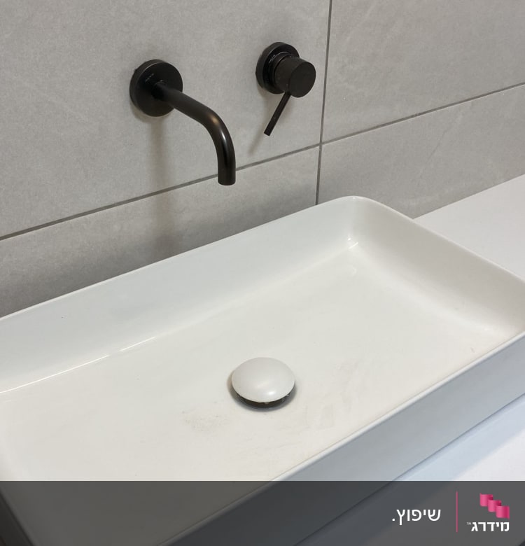 כיור מלבני עם ברז שחור על קיר אריחים