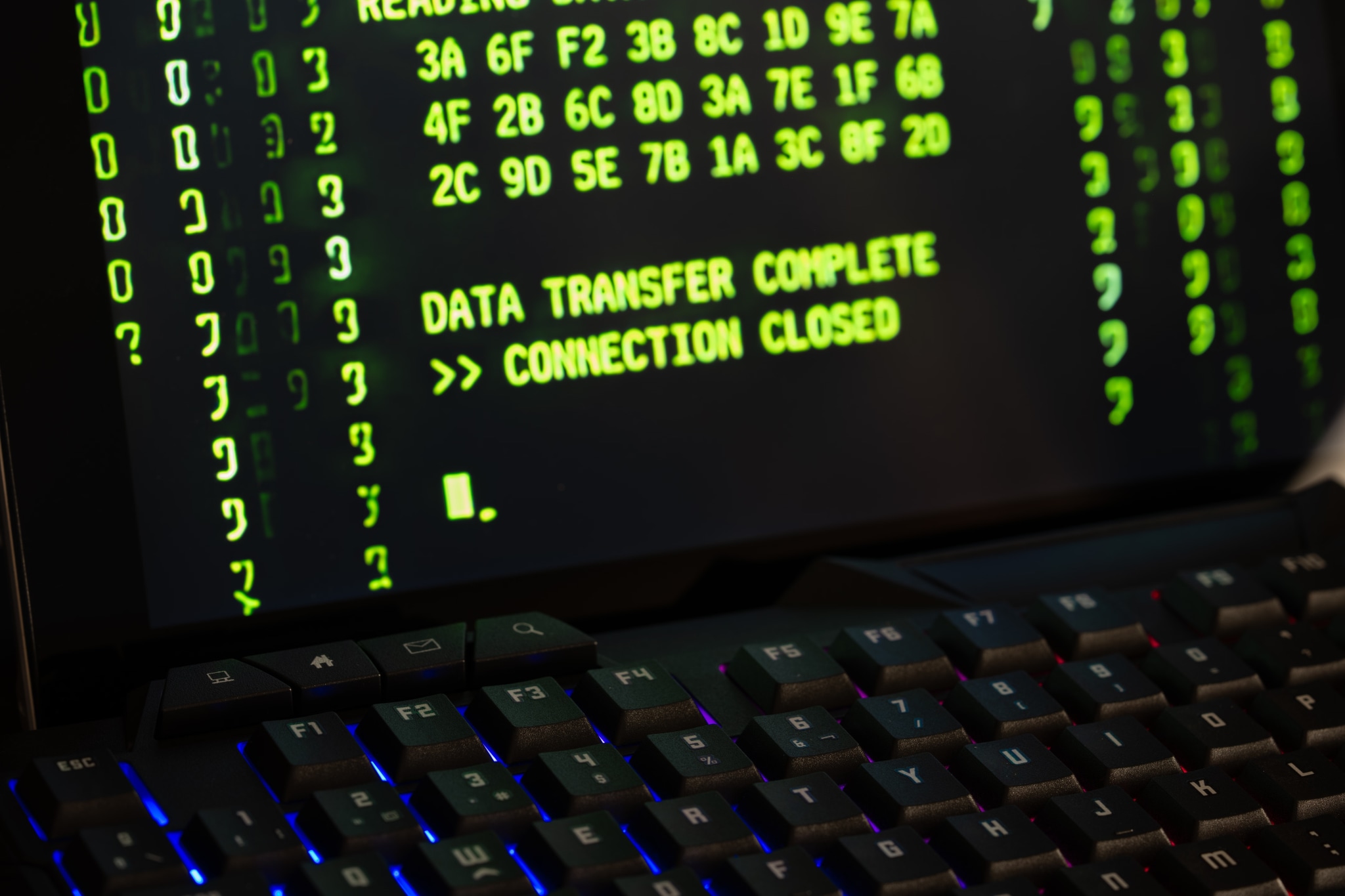 A terminal screen reading “DATA TRANSFER COMPLETE — CONNECTION CLOSED” above a backlit keyboard.