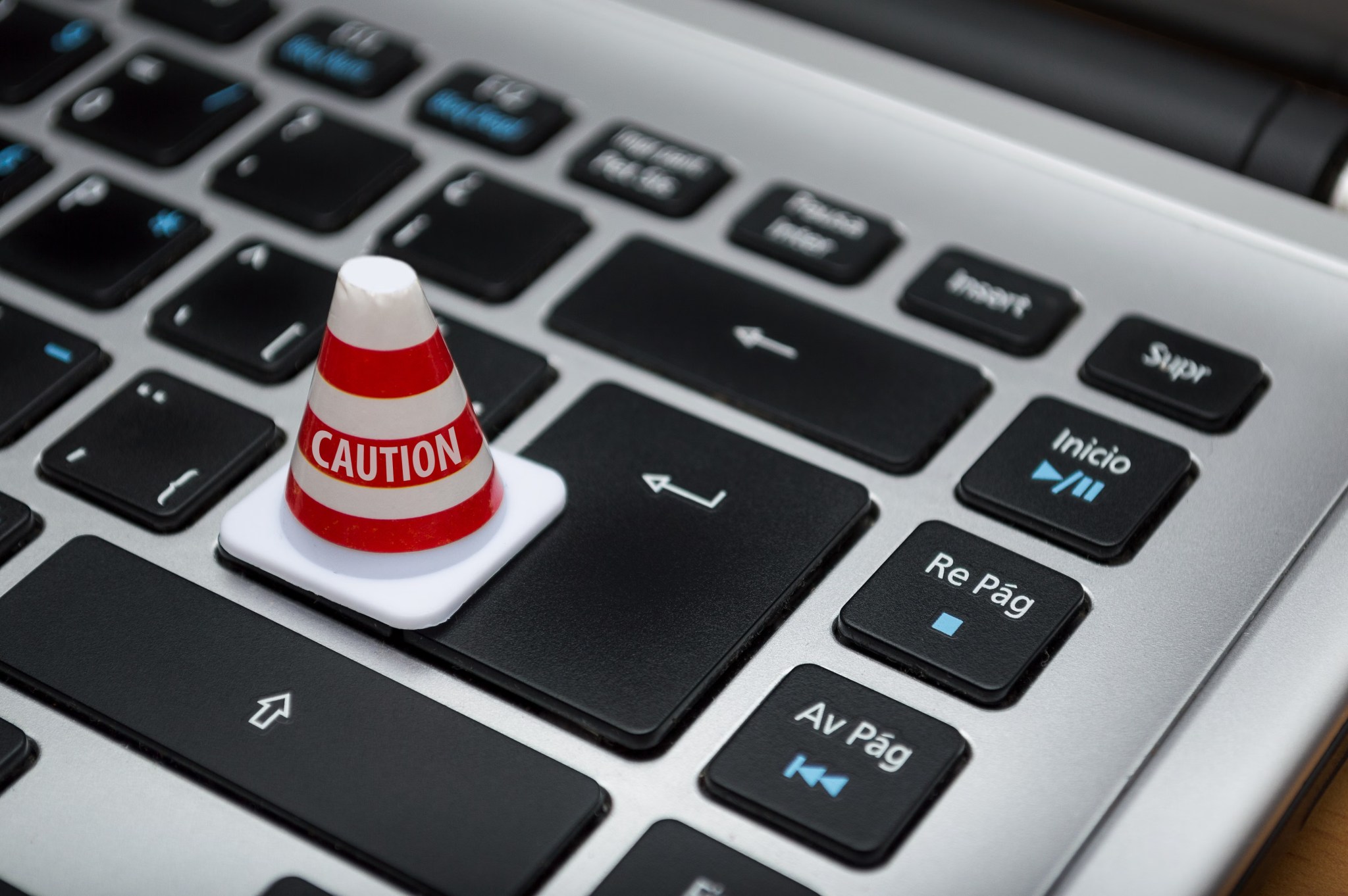 A miniature red-and-white CAUTION cone standing on the Enter key of a laptop keyboard.