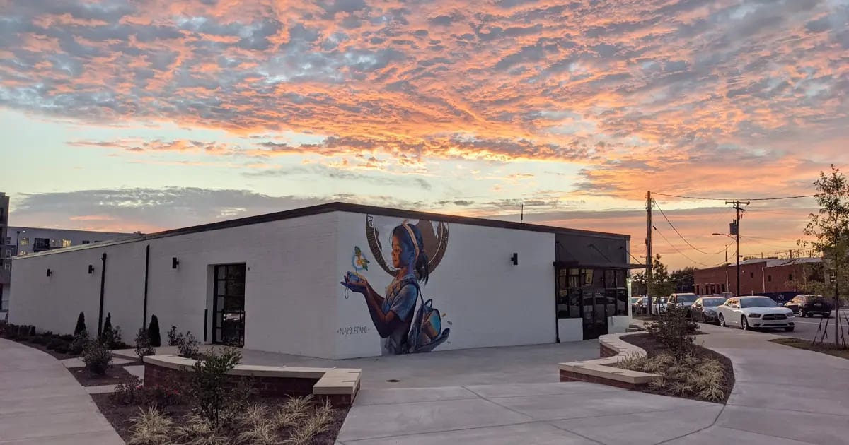 photo of a sunrise over a white brick building with a graffiti portrait painted on its side