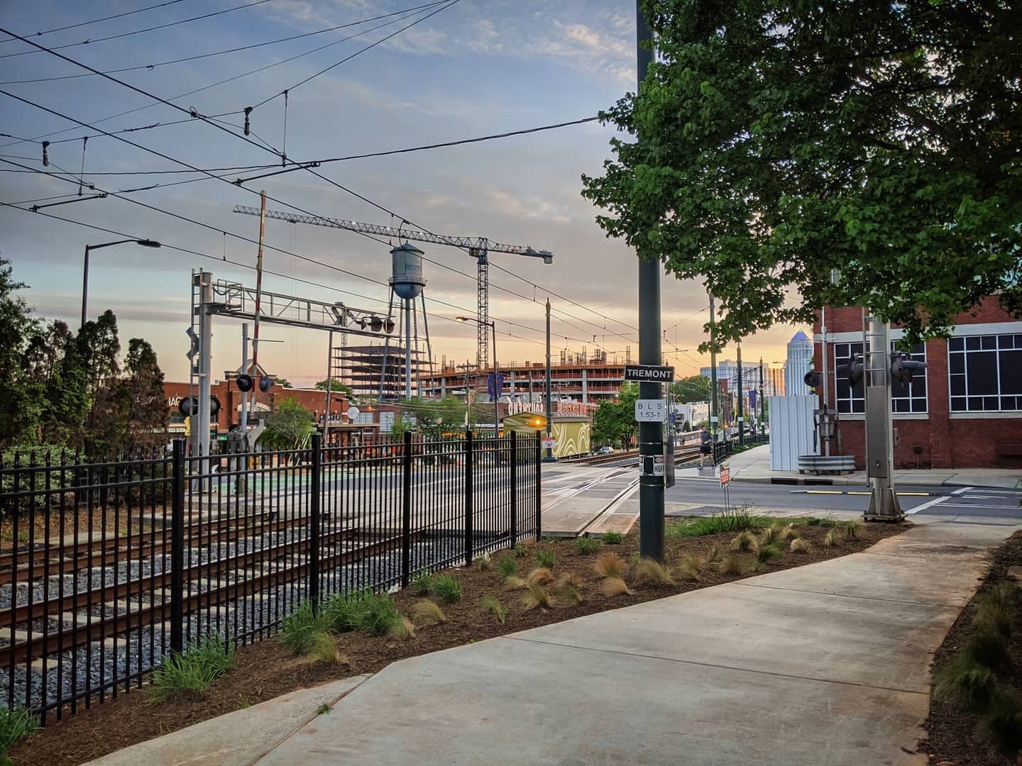 A photo of light rail tracks and a water tower, with a light colored sunrise in the background.