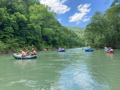 River rafts full of people floating on the blue green waters of the Big Piney Creek.