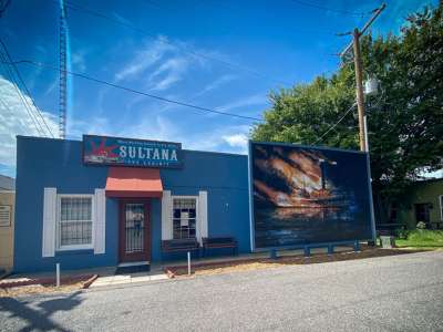 A small blue building is marked as “Sultana: The Exhibit.” Featured prominently, a mural shows the flaming Sultana burning on the water.