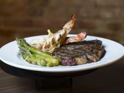 White plate with grilled steak and lobster tails with asparagus side.