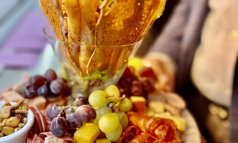 Assorted meats, cheese, olives, and crackers on a platter presented by a server.