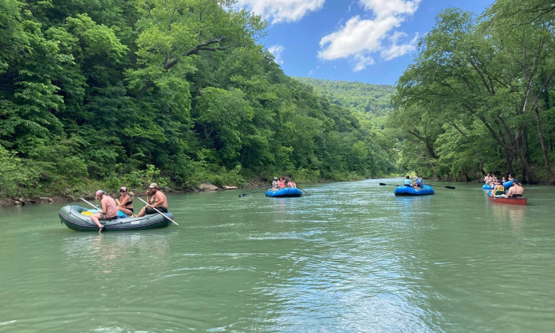 River rafts full of people floating on the blue green waters of the Big Piney Creek.