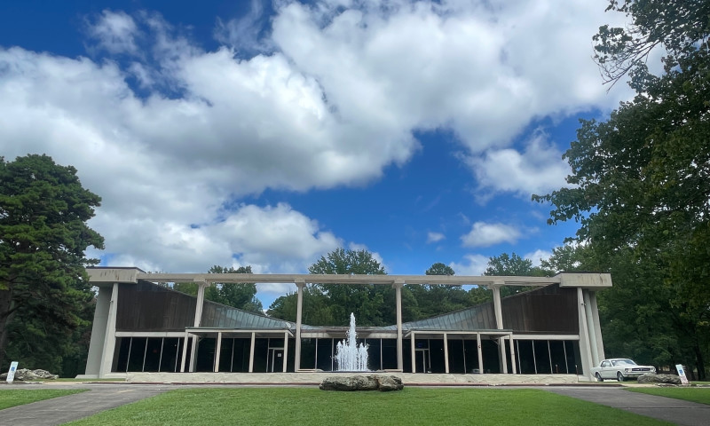 Large building with fountain out front and a green lawn under a blue sky with clouds.