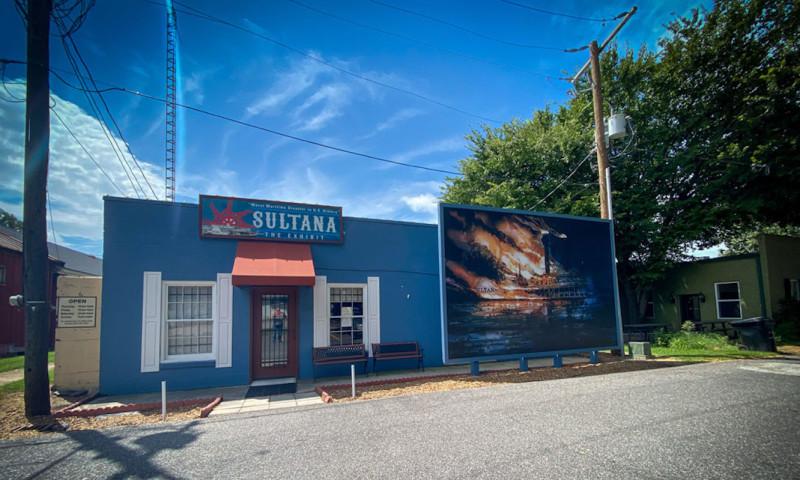 A small blue building is marked as “Sultana: The Exhibit.” Featured prominently, a mural shows the flaming Sultana burning on the water.