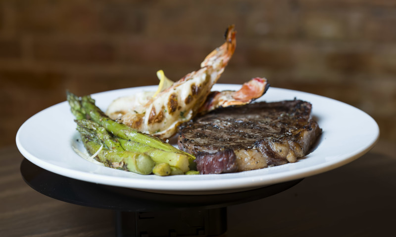 White plate with grilled steak and lobster tails with asparagus side.