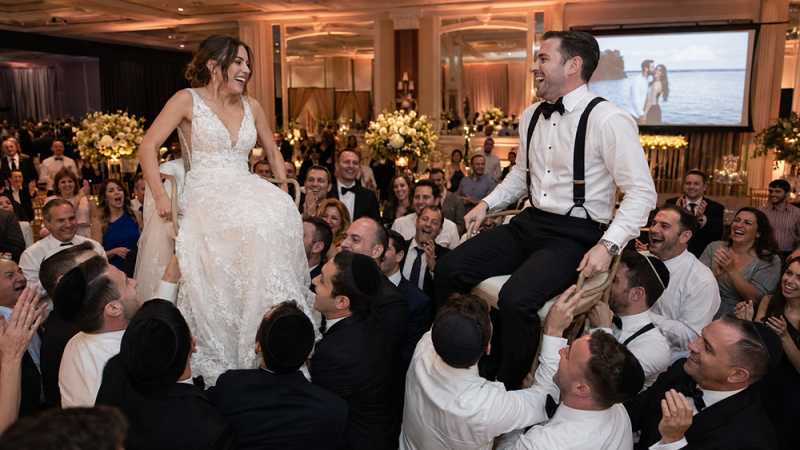 Jewish bride and groom dance the hora while a slideshow plays in the background