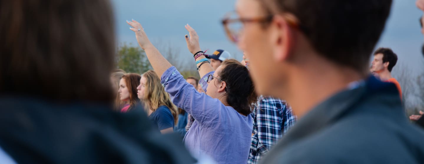 Student with hands raised at outdoor worship