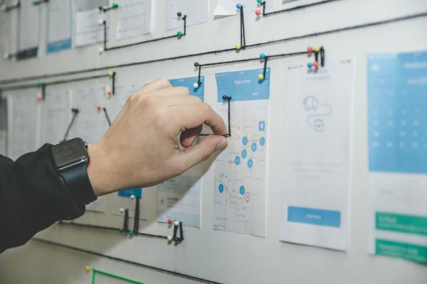 Photo of a hand reaching for a whiteboard that has a lot of papers with text and diagrams attached to it