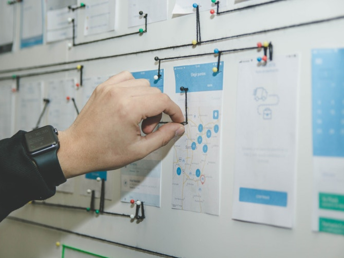 Photo of a hand reaching for a whiteboard that has a lot of papers with text and diagrams attached to it