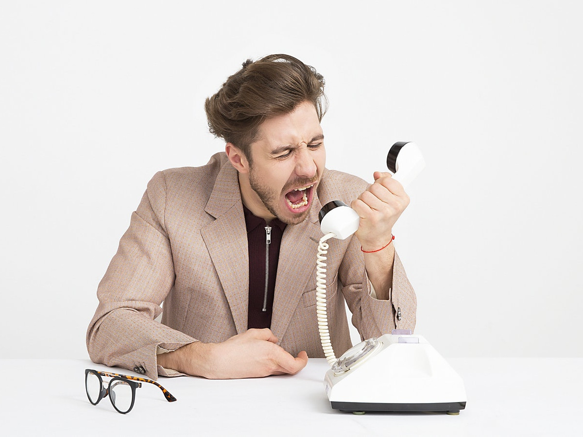 Photo of a man in a suit yelling at a phone receiver