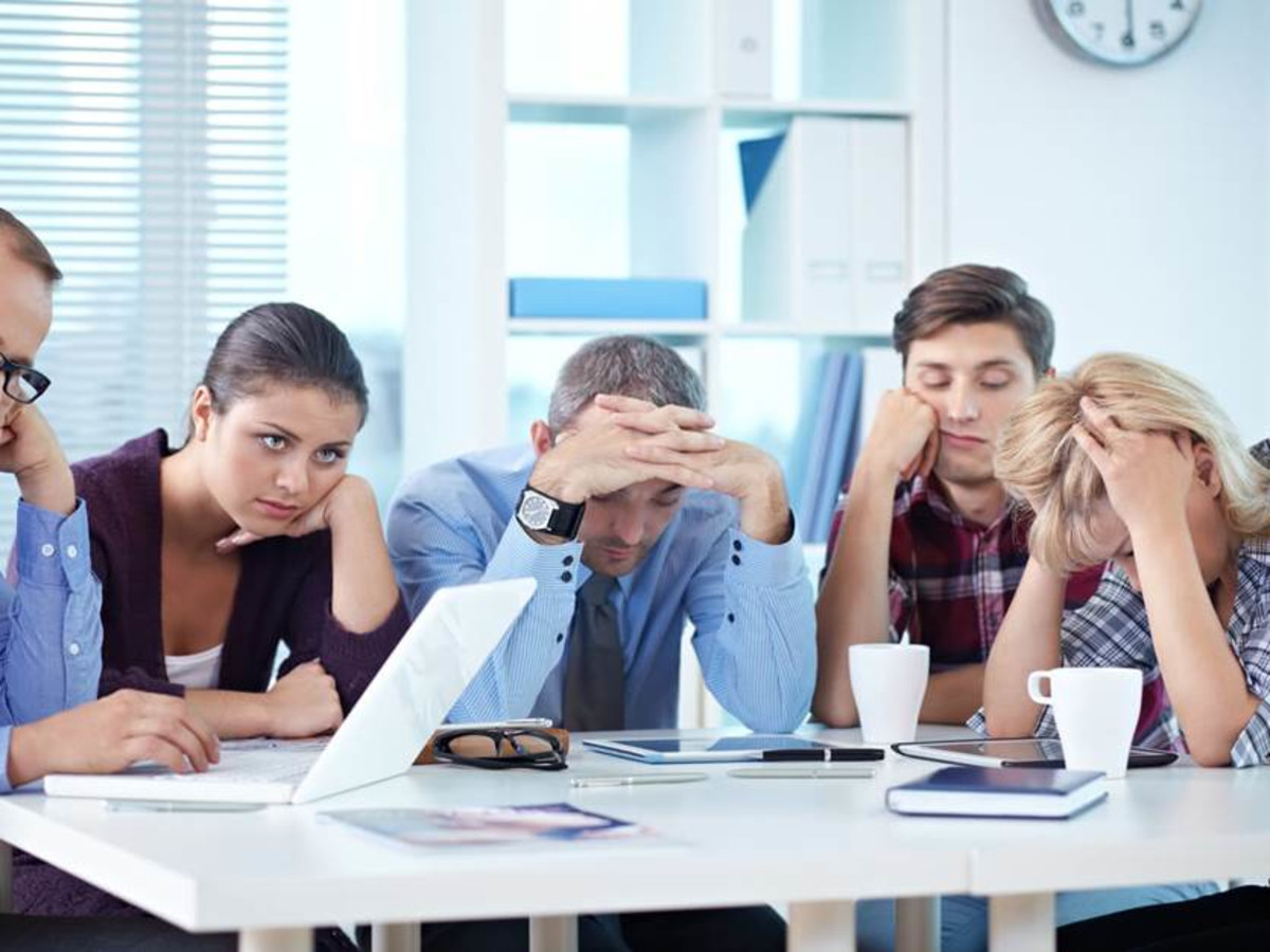 Photo of five dispirited office people sitting around a meeting table