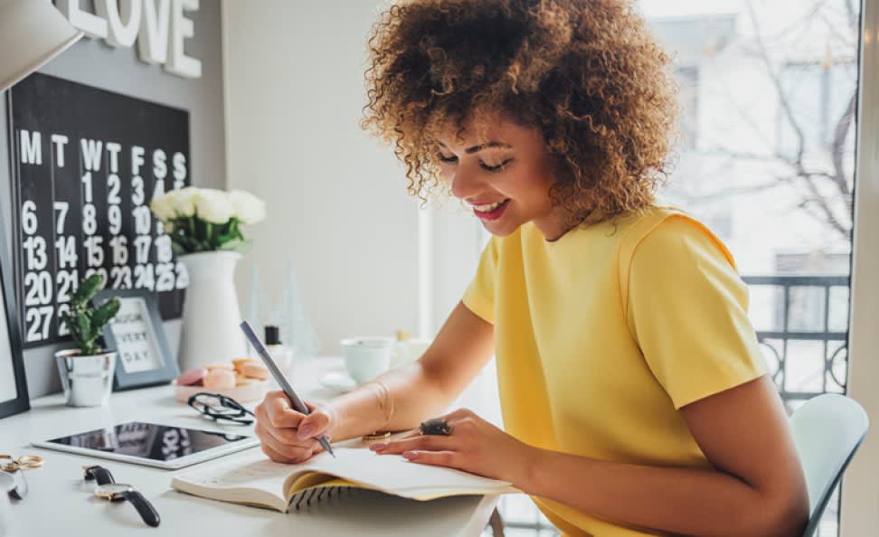 African woman sitting at her desk and writing in her notebook wearing a yellow dress
