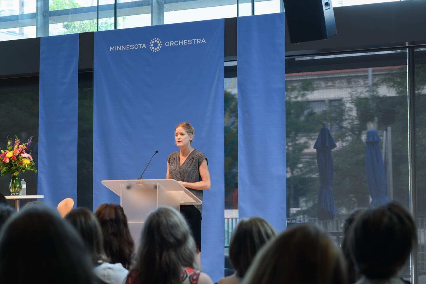 A woman--Kristen Bruya--giving a speech on a stage; audience members are pictured in the foreground.