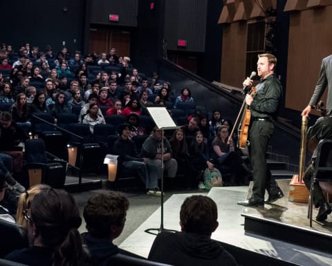 Sam Bergman speaking to a crowd in a high school auditorium