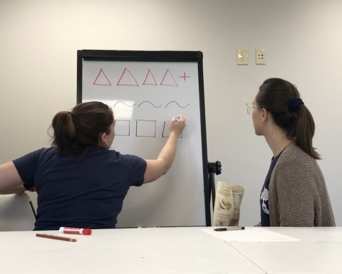 Two people writing on a white board